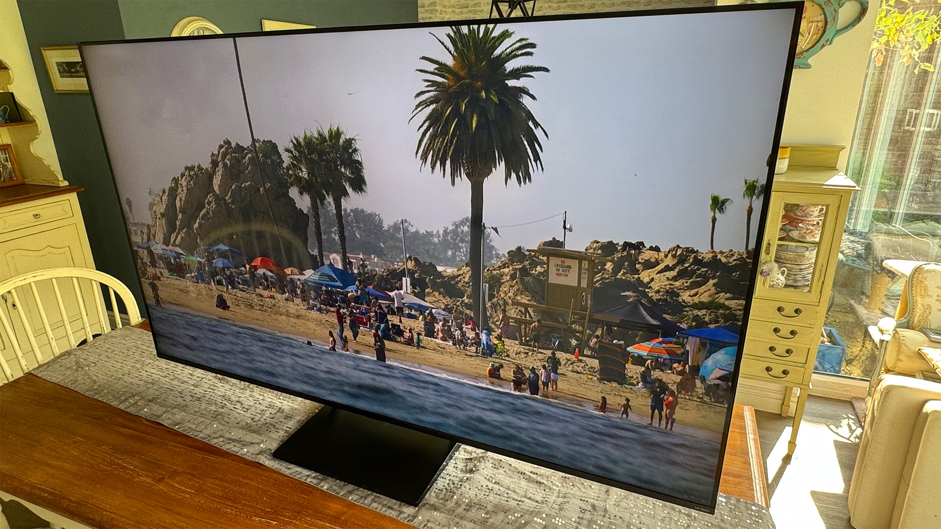 LG 65QNED93 LCD TV on wooden dining table slight angle, on screen is beach scene