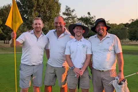 Ben Read Jonathon Wallace, Mike Ashwin, Ben Read, and Ben Smith pictured at Chipping Sodbury Golf Club, wearing white polo shirts and khaki shorts, standing on the green after completing their16-hour golf challenge with rolling fairways and trees behind them.