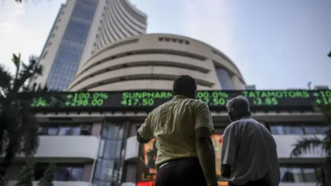 Getty Images Pedestrians look up at an electronic screen and a digital ticker board at the Bombay Stock Exchange building in Mumbai.