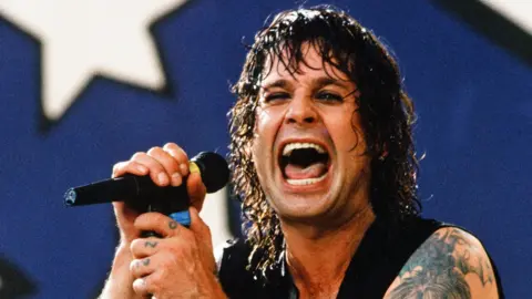 Getty Images Ozzy Osbourne holding a microphone on stage, drenched in sweat and with a maniacal smile