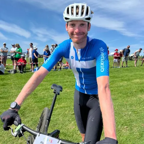 Man wearing a blue top, white helmet and holding a bike