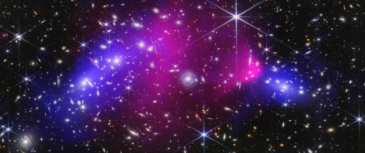 The central region of the Bullet Cluster, made up of two massive galaxy clusters. Galaxies and stars were captured by the James Webb Space Telescope. Hot X-rays captured by the Chandra X-ray Observatory appear in pink. Blue represents the dark matter, which was mapped by scientists using Webb’s imaging. Credit: NASA, ESA, CSA, STScI, CXC. Science: James Jee (Yonsei University, UC Davis), Sangjun Cha (Yonsei University), Kyle Finner (Caltech/IPAC)