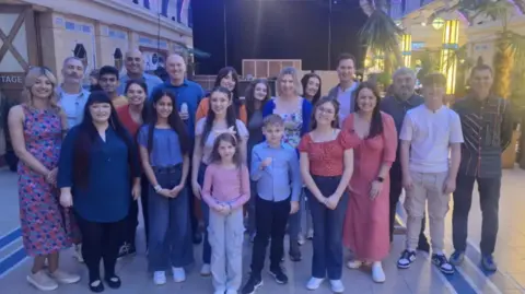 Stephanie Nelson Another group picture of the stammering choir. There are three rows in height order and they are smiling at the camera.