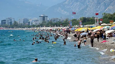 Getty Images A beach in Turkey where lots of people are sunbathing under umbrellas, and many other people are swimming in the sea