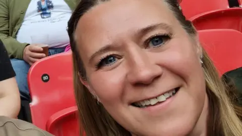 Michelle Brown A woman smiling and looking directly at the camera. There are red seats behind her. 