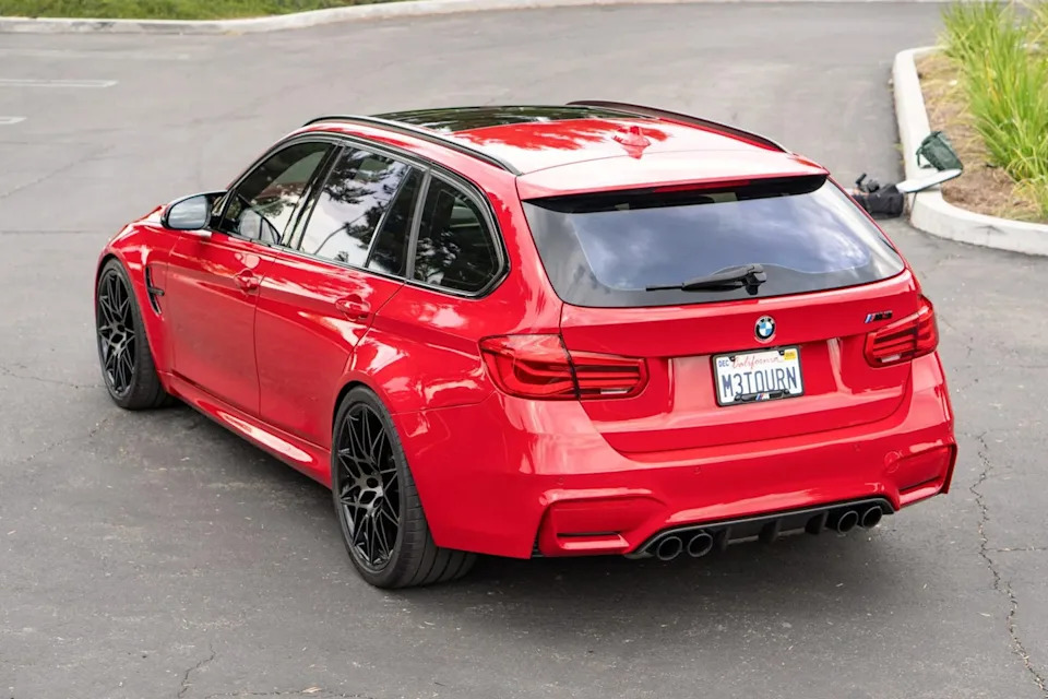 rear side view of red station wagon with roof spoiler, quad exhaust tips, and tinted windows parked on pavement.