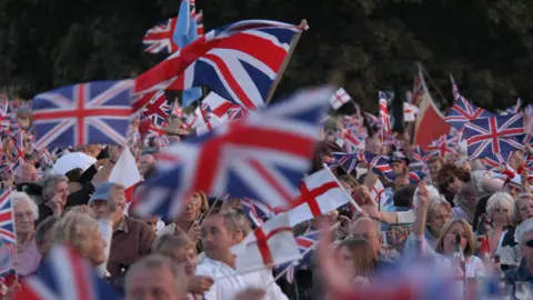 Bedford Proms A large crowd of people waving flags at a Proms event.