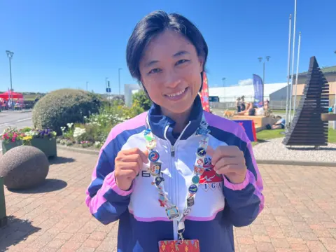Woman holding a lanyard, displaying various different pin badges
