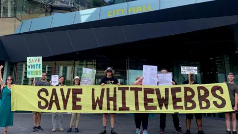 Guardians of Whitewebbs Protesters holding signs and a large yellow banner reading “Save Whitewebbs” demonstrate outside London’s City Hall against plans to build a Tottenham Hotspur training ground in the park.