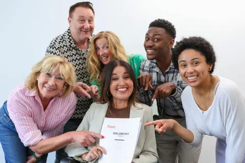 The members of the new balamory cast gather round pointing to a script that says 'Balamory'