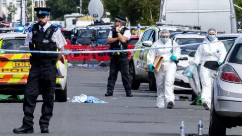 PA Media There is a police cordon on Hart Street. Two forensic investigators wearing white overalls and masks are walking within the police cordon. There are two officers also standing guard at the scene.