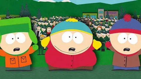 Comedy Central/Facebook South Park cartoon characters Kyle, Eric and Stan (standing from left to right) standing in front of a crowd of people. The trio have shocked expressions on their faces and their arms are raised. 