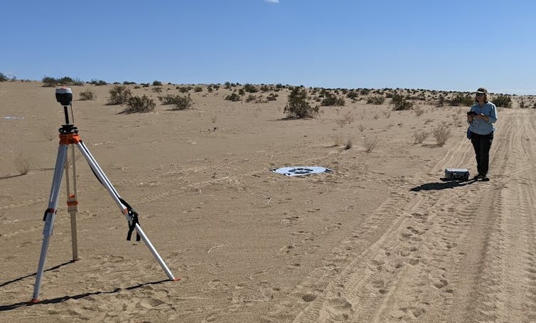 A woman in the desert, near a tripod and a GPS target.