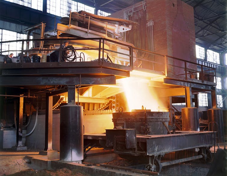 Bright hot metal pouring out of a large metal furnace.