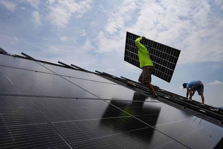 Workers install solar panels on a roof.