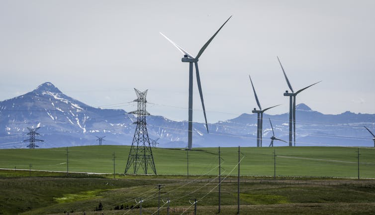 Wind turbines and transmission towers in a field with snowcapped mountains in the background