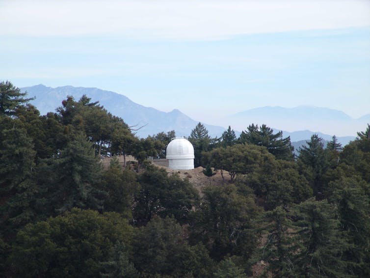 A white-domed building on a hilltop among trees.