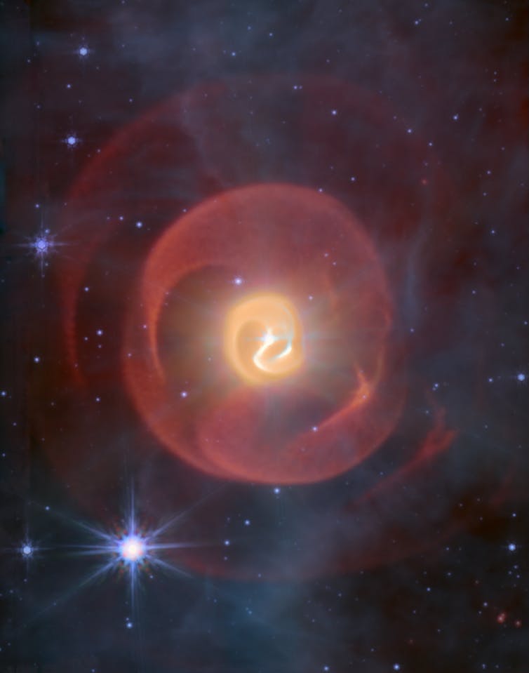Three shells of dust, looking like coiled snakes, the middle one yellow and the outer ones red against a background of blue stars.