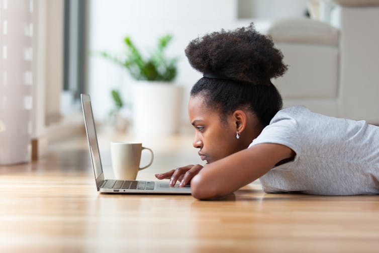A teenage girl lying on the ground using a laptop.