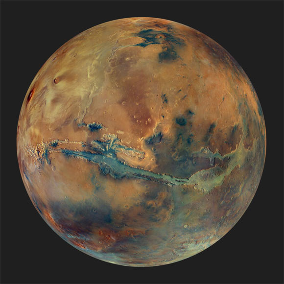 This image from Mars Express’ High Resolution Stereo Camera shows the globe of Mars set against a dark background. The disk of the planet features yellow, orange, blue and green patches, all with an overall muted grey hue, representing the varying composition of the surface. Image credit: ESA / DLR / FU Berlin / G. Michael / CC BY-SA 3.0 IGO.