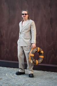 PARIS, FRANCE - JUNE 25: A guest wears black sunglasses, gold necklace, light brown double breasted blazer jacket, light brown loose Louis Vuitton trouser pants, shiny black platform boots leather shoes. dark brown Louis Vuitton lifebuoy canvas bag, Louis Vuitton bag turtle bag charm, Louis Vuitton starfish bag charm, outside Louis Vuitton, during the Paris Fashion week Men's Spring/Summer 2026 on June 25, 2025 in Paris, Franco (Photo by Edward Berthelot/Getty Images)