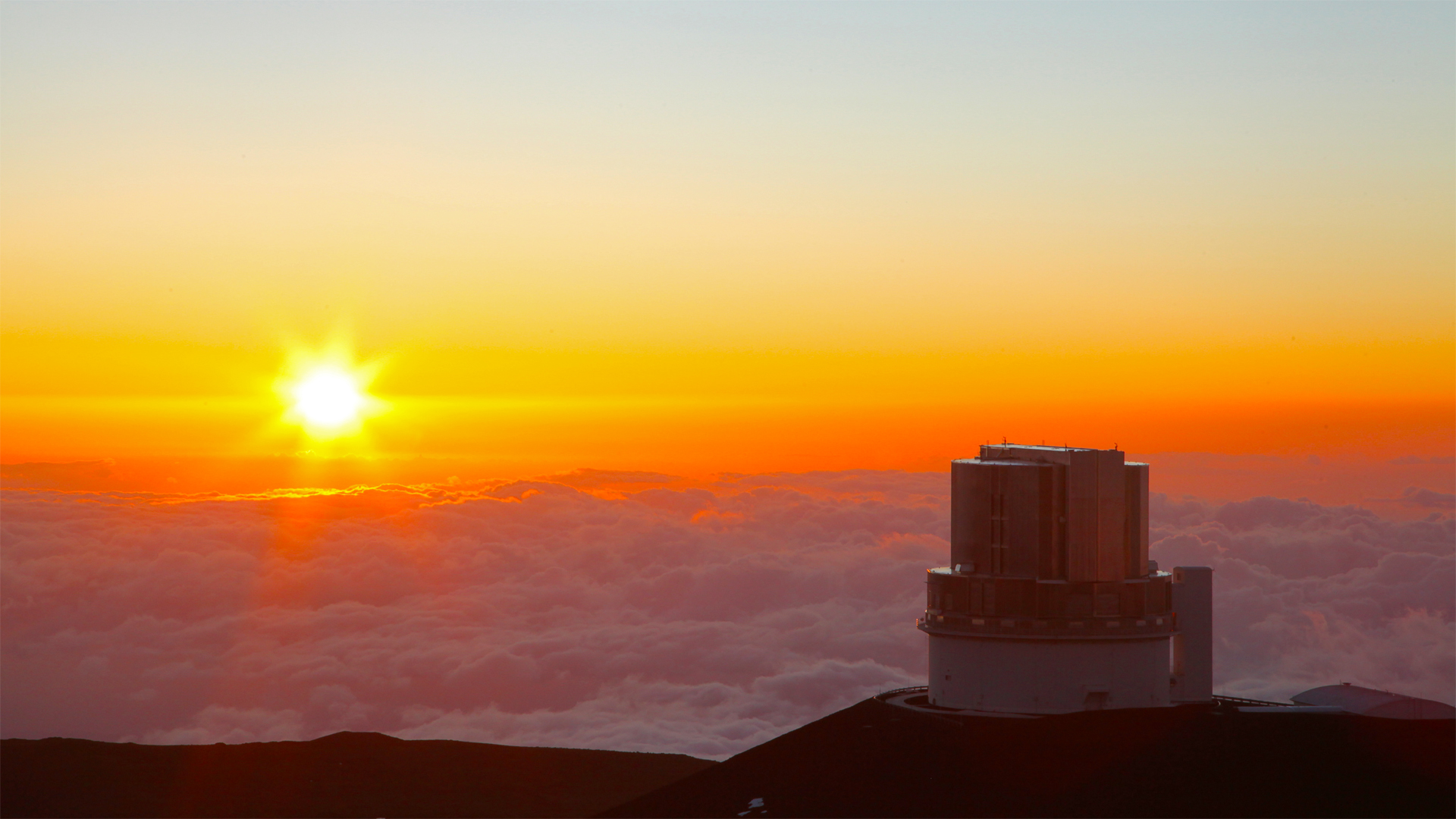 a round building a top a mountain, sitting above cloud cover