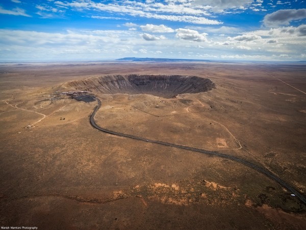 Large crater in a desert landscape, with a road in the foreground.