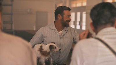 A man holding a terrier dog in his arms smiling, laughing and looking off to the side