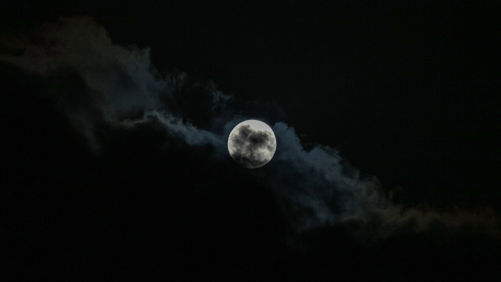A full moon is pictured against a dark sky, partially covered by clouds