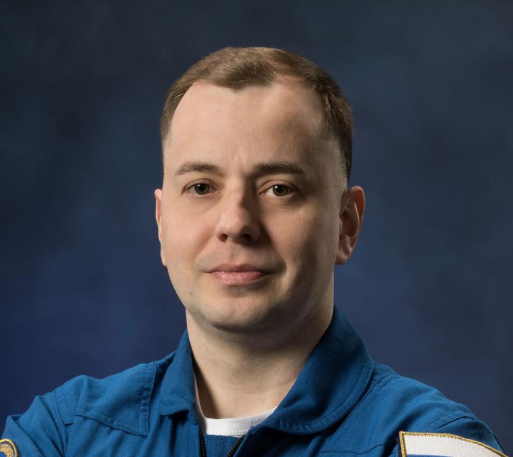 a man in a blue flight suit poses for a portrait
