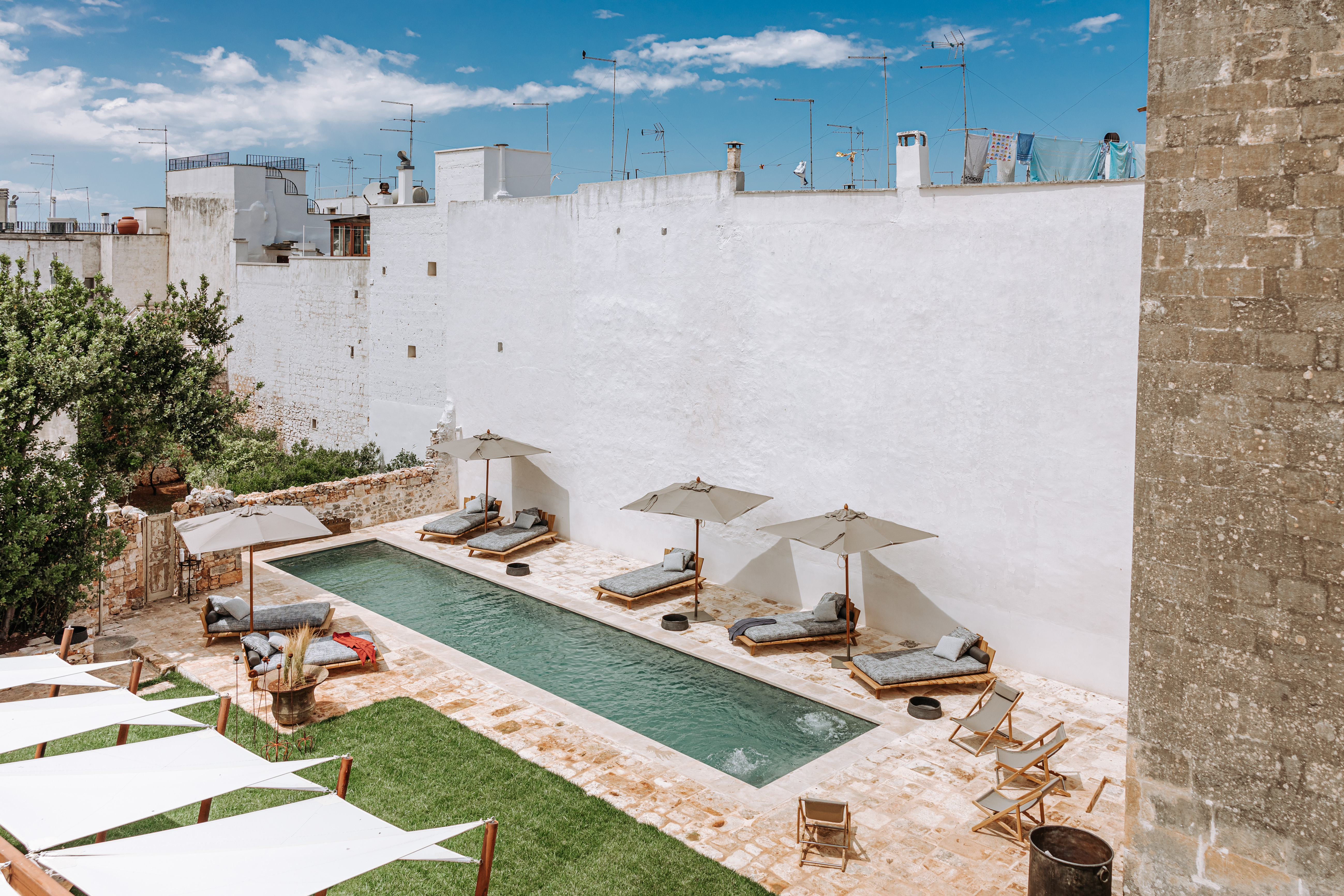 Rectangular pool with lounge chairs and umbrellas in a courtyard.