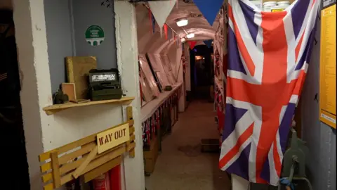 BBC Inside the underground air raid tunnel museum under Clifford Primary School in Ipswich. War memorabilia sits inside the tunnel including a union jack flag/