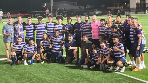Marshall Islands Soccer Federation The Marshall Islands' first international team pose for a group shot after facing off the US Virgin Islands on Thursday in Springdale, Arkansas. They are at the pitch, looking away from the camera.