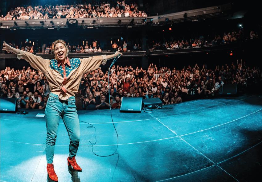 Whitney Cummings on stage on her Big Baby tour with the crowd behind her