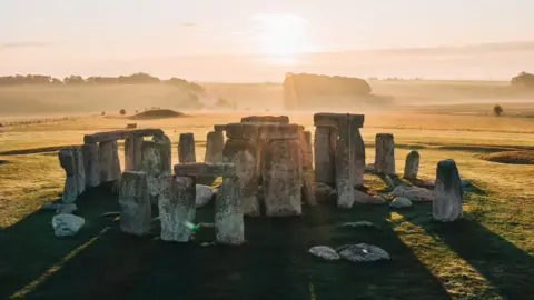 Getty Images Stonehenge seen with the sun behind and sun beams streaming through the large stones placed in a circle and lighting up the hills and fields behind.