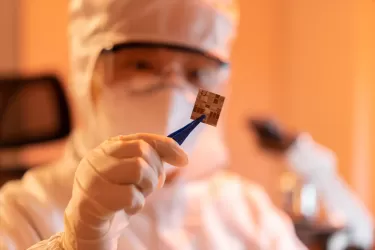Man in protective clothing holding a silicon chip in tweezers