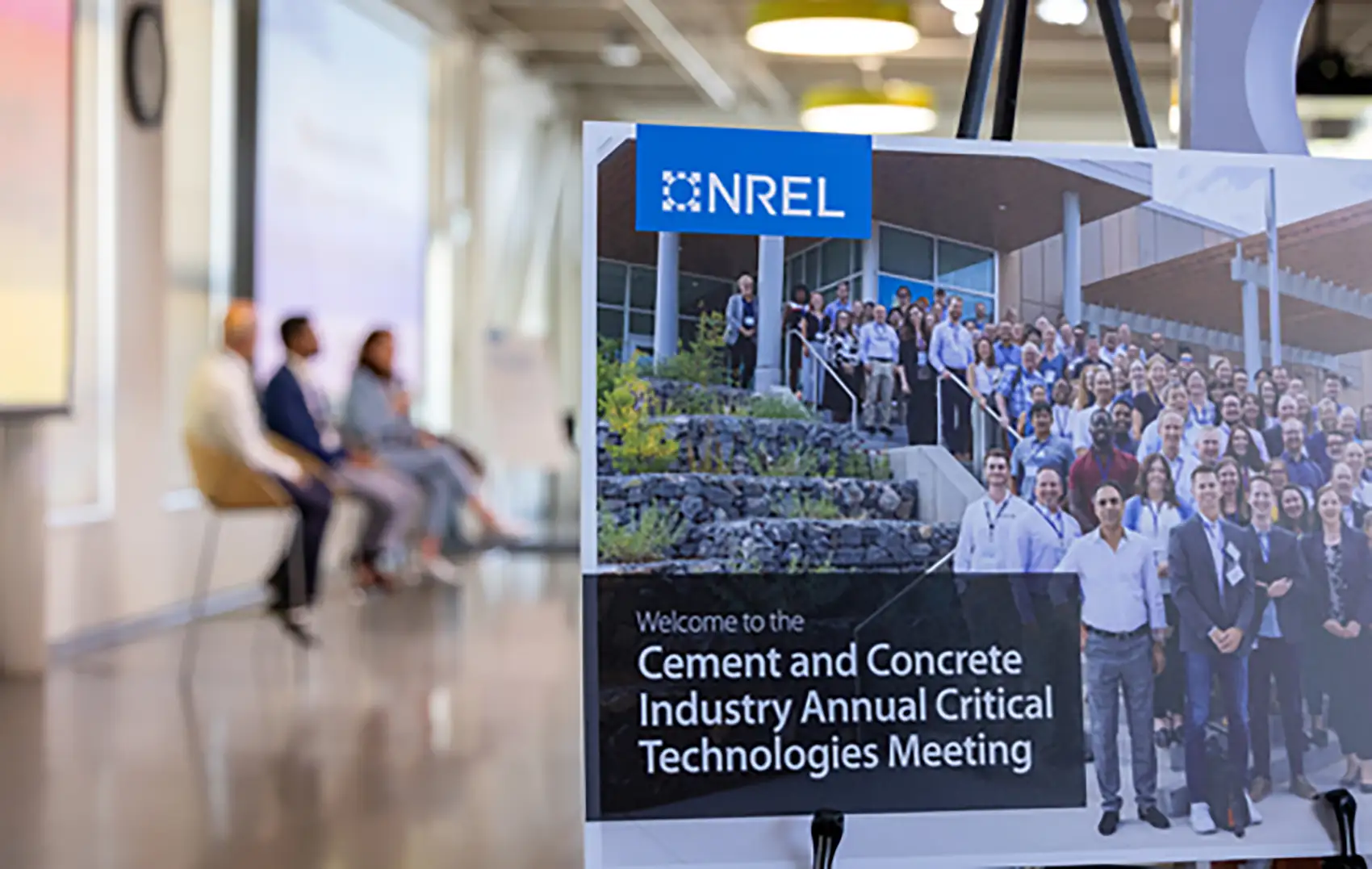 20250820-paving-the-road-for-cement-and-concrete-technologies-100859 Close up of a sign that says “Welcome to the Cement and Concrete Industry Annual Critical Technologies Meeting” with a panel of three individuals in the background.