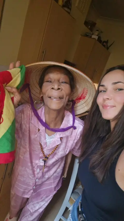 Vasilisa Ermakova Marline Anderson, a 77-year-old woman in a Vietnamese sun hat, smiles next to a Vasilisa, a young woman with long dark hair