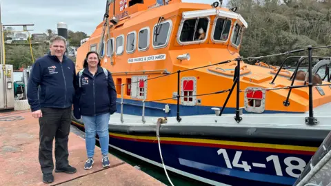 Allan Thornhill Allan and Helen Thornhill standing on a jetty next to the RNLI lifeboat in Fowey in Cornwall