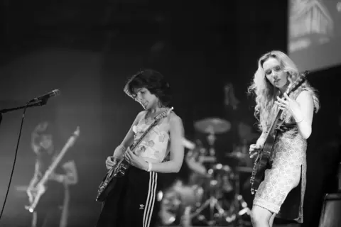 Dr David Gange Two female members of Meatdripper are seen on stage in a black and white image. They both have guitars.