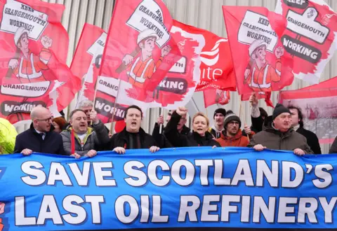 PA Media Unite General Secretary Sharon Graham at the centre of a line of workers shouting in protest outside the oil refinery. They all hold up large union flags at the demonstration in February 2025