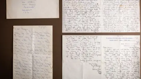 Bearnes Hampton & Littlewood The image shows an enveloped addressed to Reggie Kray in prison on the Isle of Wight, with a letter beneath. On the right there is a photo of a letter Reggie write to his mother Violet. It is on Brixton Prison headed paper and bears  his prison number 058111.  The front of a letter Reggie Kray wrote to his twin Ronnie from Parkhurst Prison on the Isle of Wight is also photographed. It has a date stamp 3 July 1982.