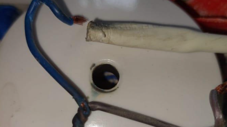 A frayed blue wire which has detached from a dirty plastic white wire cover. The bottom of the blue wire has also become twisted with a brown wire.