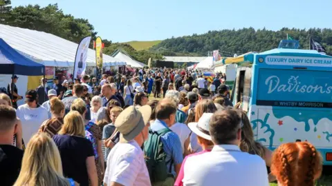 ROYAL MANX AGRICULTURAL SHOW Crowds of people in summer clothes among the marquees and an ice cream van on the show field.