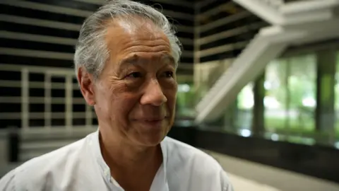 BBC/ Lulu Luo A grey-haired Richard Han is smiling as he talks to the BBC. He is wearing a white shirt.