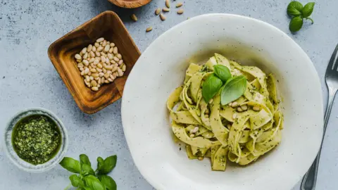 Getty Images A plate of pesto pasta accompanied by a bowl of pine nuts and a sprig of basil