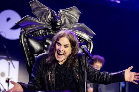 Ross Halfin A seated Ozzy Osbourne wears dark eye make-up and a dark leather jacket at the Villa Park gig. His throne has a bat at the head.