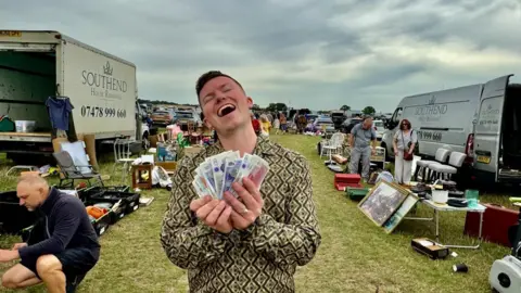 Sonny Green A man in the middle of a car boot sale holding a wad of cash with his eyes closed