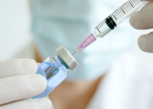 doctor's hand holds a syringe and a blue vaccine bottle at the hospital. Health and medical concepts