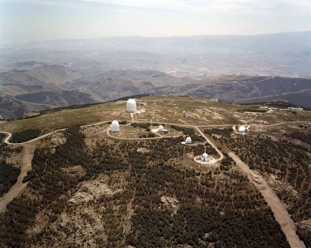 Aerial view of the Calar Alto Observatory from the north at the telescope domes. From left to right: the 2.2-m telescope, the Spanish 1.5-m telescope (in the foreground), the 1.2-m telescope, the Schmidt-reflector and the dome of the 3.5-m telescope with a height of 43 m. In the background the coast of Almería is seen. Credit: MPIA